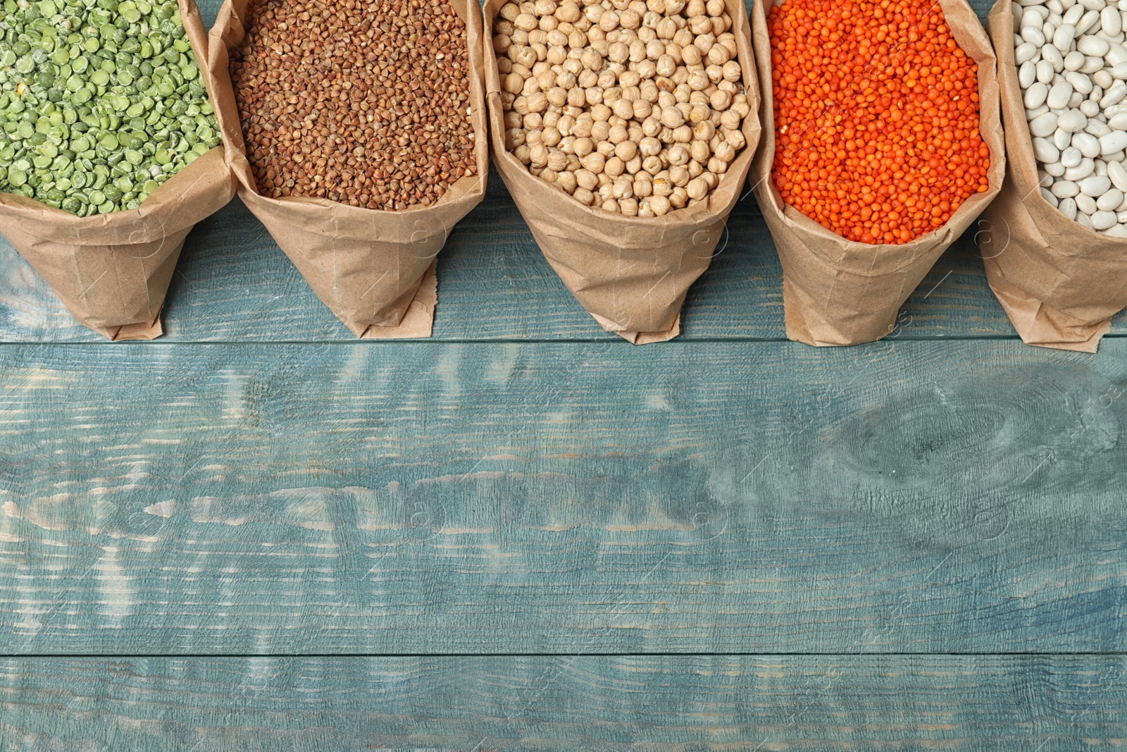 Photo of Flat lay composition with different types of legumes and cereals on blue wooden table, space for text. Organic grains