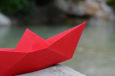 Photo of Beautiful red paper boat on stone outdoors, closeup