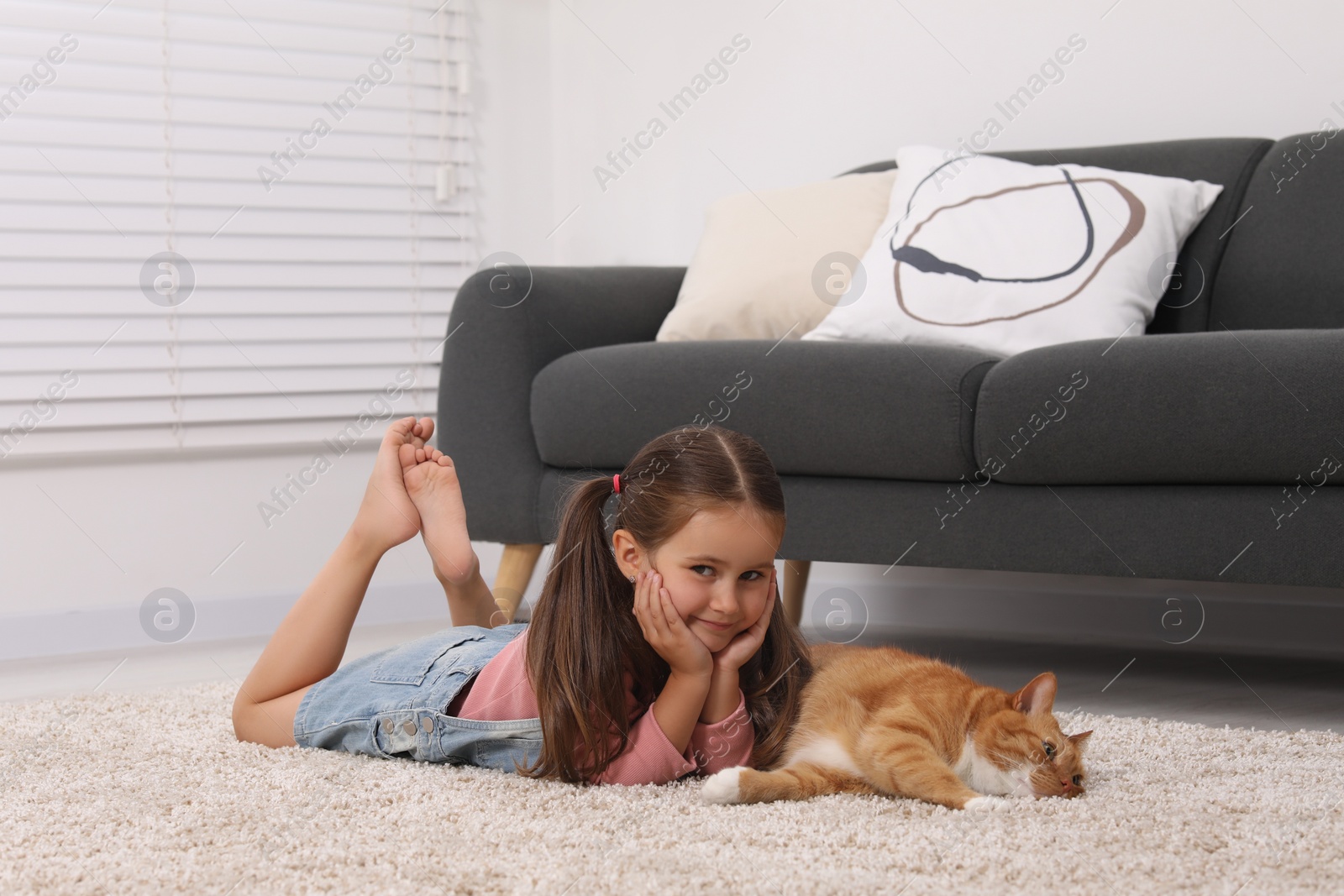 Photo of Smiling little girl and cute ginger cat on carpet at home