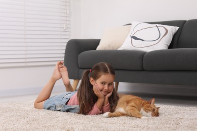 Smiling little girl and cute ginger cat on carpet at home