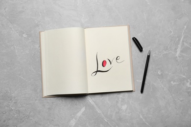 Photo of Open notebook with handwritten word Love near pen on light grey table, flat lay