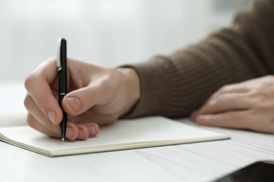 Photo of Man writing in notebook at white wooden table, closeup