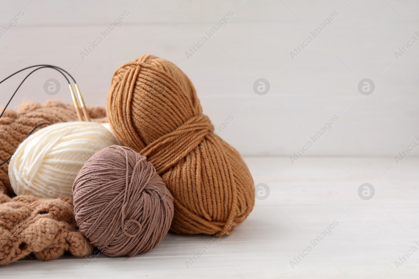 Photo of Soft woolen yarns with knitting needles and sweater on white table, space for text