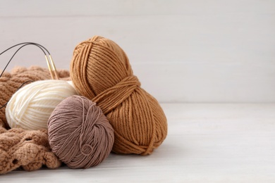 Photo of Soft woolen yarns with knitting needles and sweater on white table, space for text