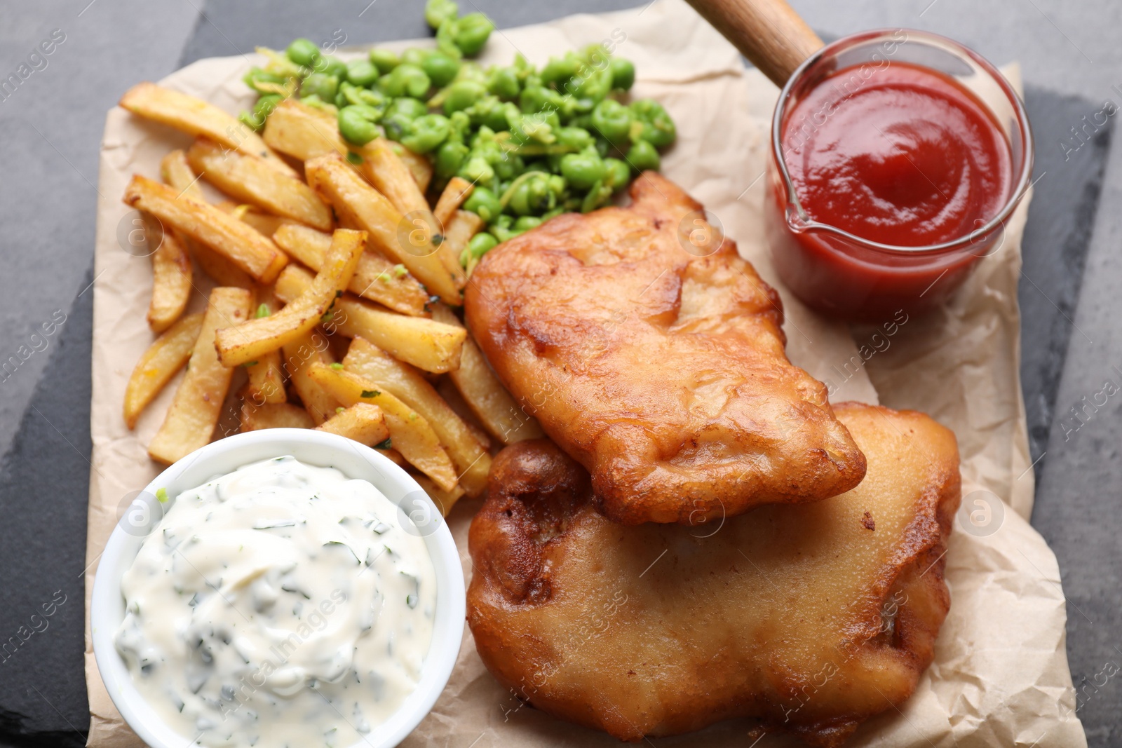 Photo of Tasty fish, chips, sauces and peas on grey table, above view