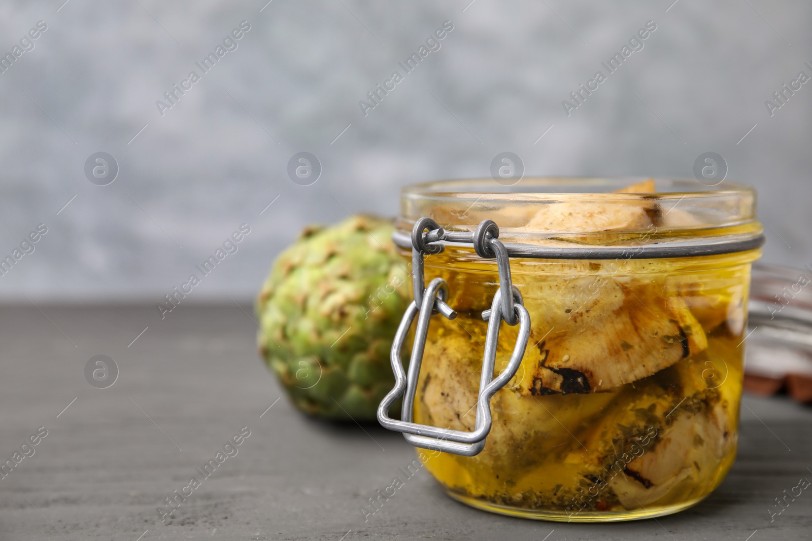 Photo of Jar of delicious artichokes pickled in olive oil on grey wooden table, closeup. Space for text