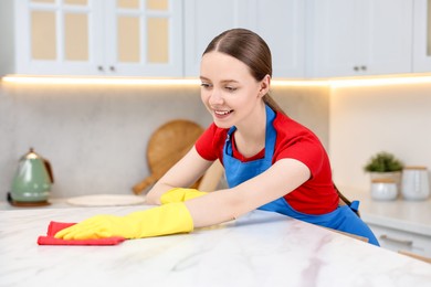 Photo of Woman cleaning white marble table with rag in kitchen