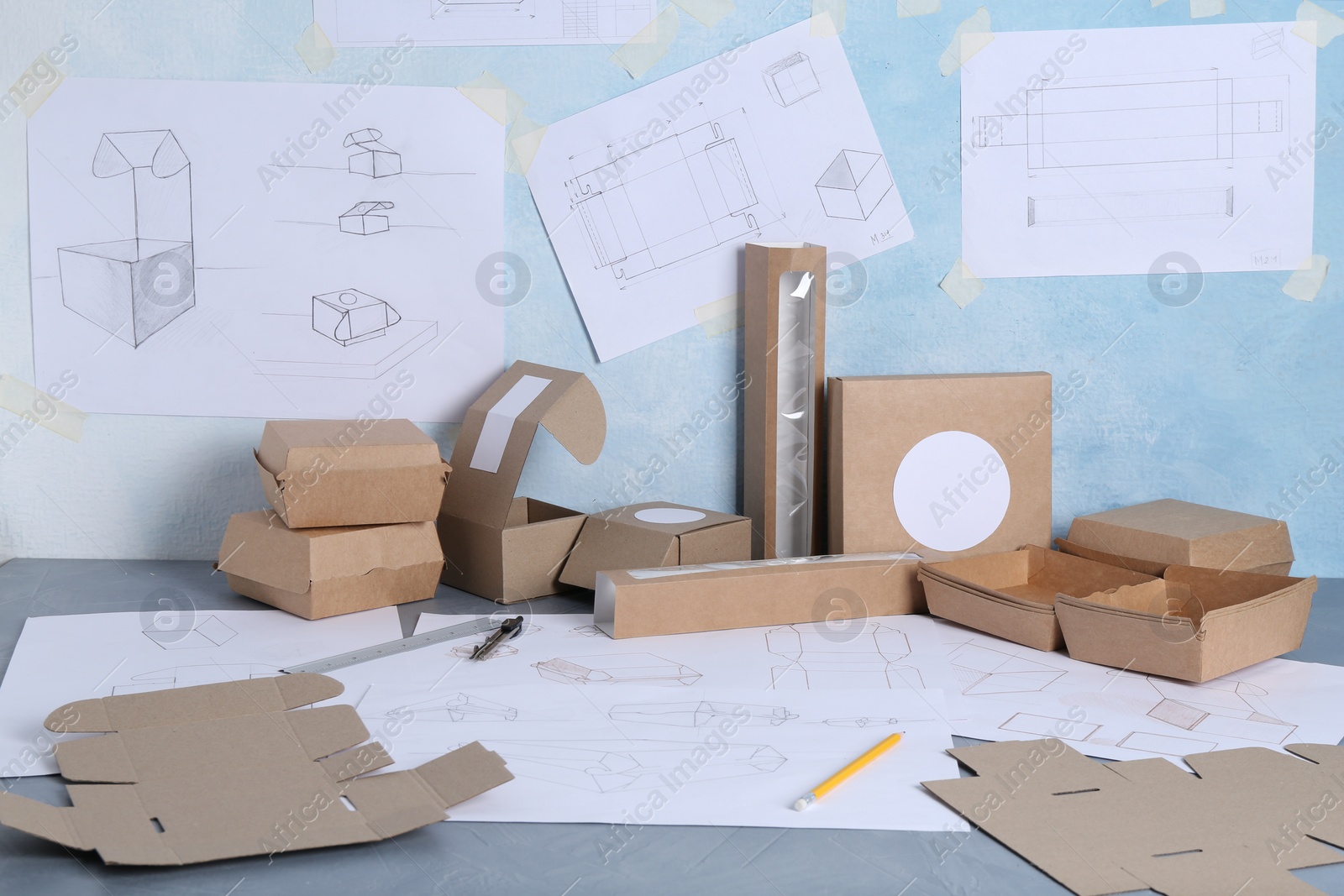 Photo of Creating packaging design. Drawings, boxes and stationery on blue textured table, closeup