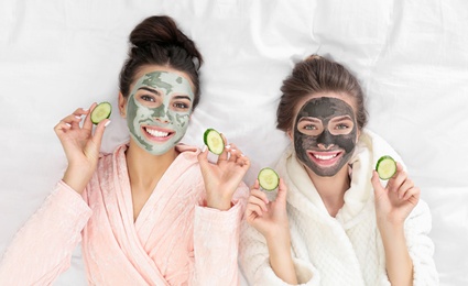 Photo of Young friends with facial masks having fun on bed at pamper party, top view