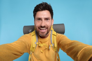 Photo of Happy man with backpack taking selfie on light blue background. Active tourism