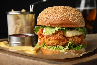 Delicious burger with crispy chicken patty, french fries and sauce on table, closeup