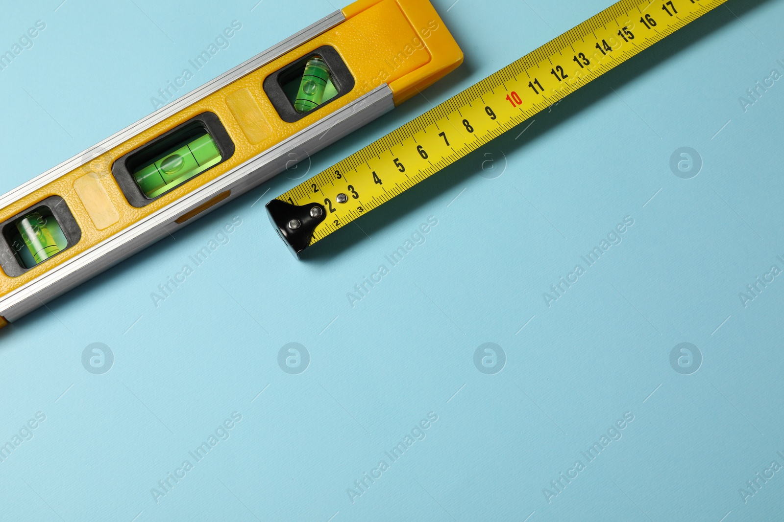 Photo of Building level and tape measure on light blue background, top view. Space for text