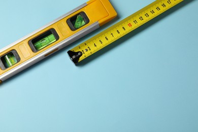 Photo of Building level and tape measure on light blue background, top view. Space for text