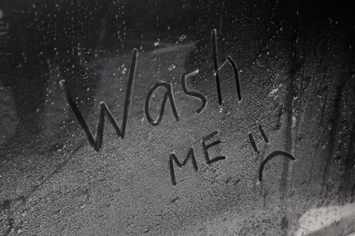 Photo of Inscription WASH ME and sad smiley on dirty car, closeup