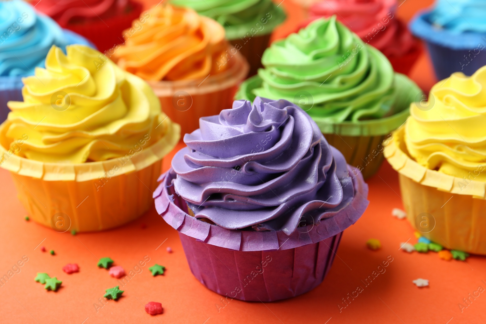 Photo of Delicious bright cupcakes and sprinkles on coral background, closeup