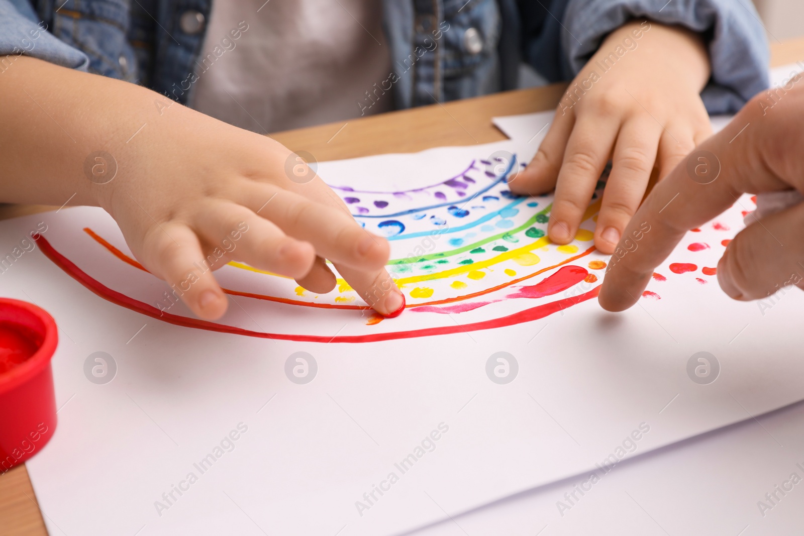Photo of Little child painting with finger at wooden table indoors, closeup