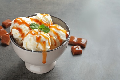 Photo of Tasty ice cream with caramel sauce in bowl on table
