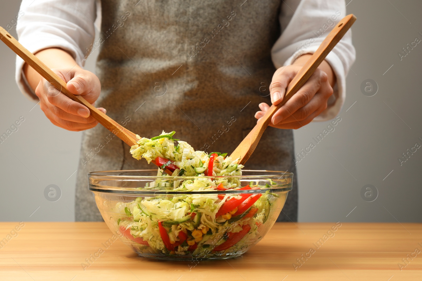 Photo of Woman making tasty salad with Chinese cabbage at wooden table, closeup