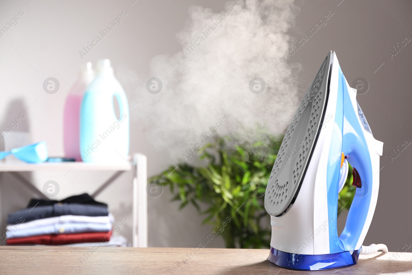 Photo of Modern iron with steam on table indoors. Space for text