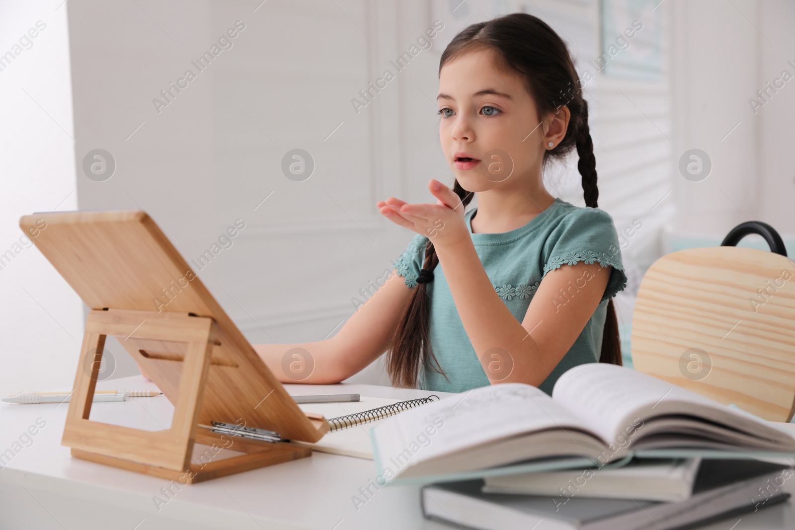 Photo of Little girl doing homework with tablet at table in room