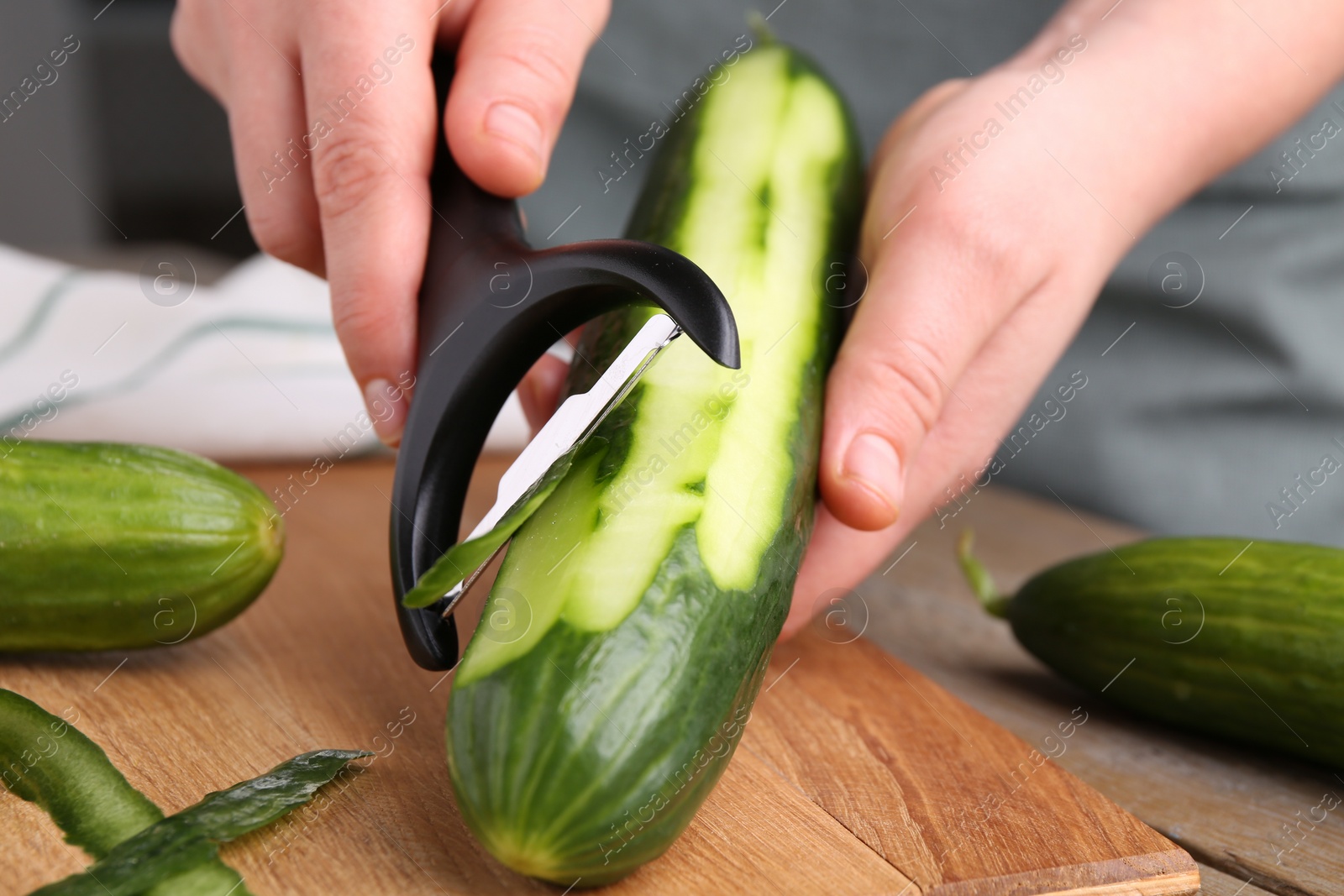 Photo of Woman peeling cucumber at wooden table, closeup