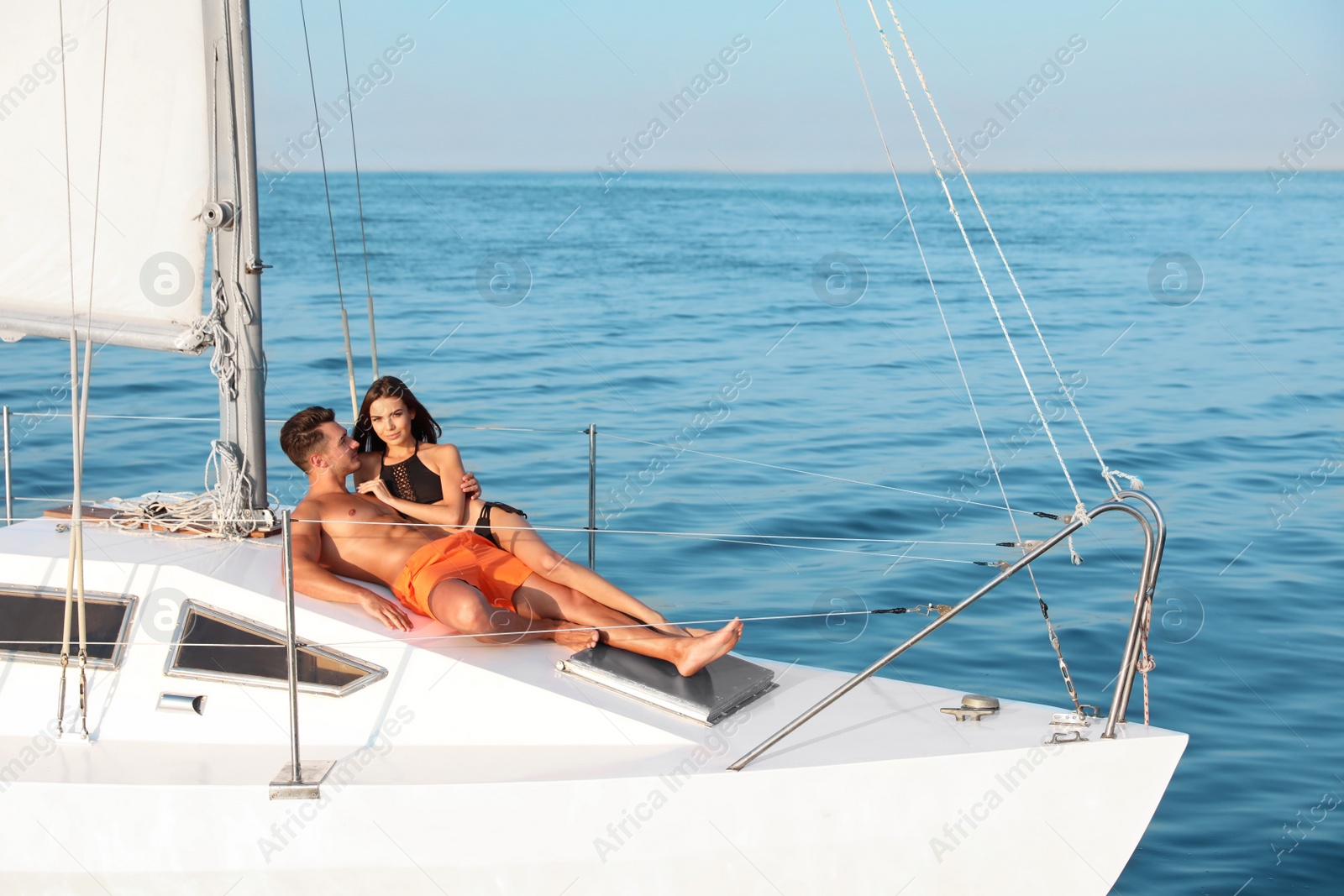 Photo of Young man and his beautiful girlfriend in bikini relaxing on yacht. Happy couple at sea