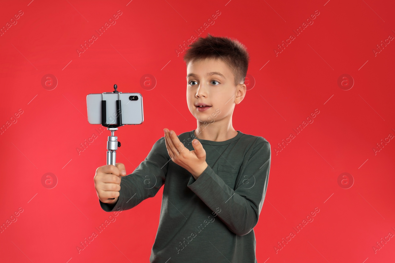 Photo of Cute little blogger recording video on red background