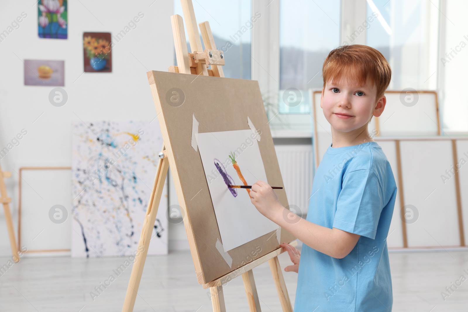 Photo of Little boy painting in studio. Using easel to hold canvas