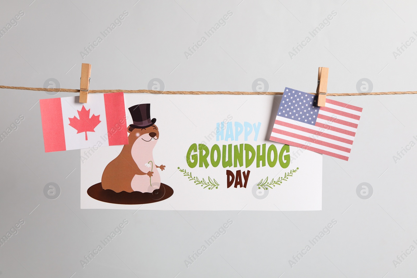 Photo of Happy Groundhog Day greeting card and flags hanging on light background