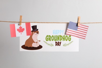 Photo of Happy Groundhog Day greeting card and flags hanging on light background