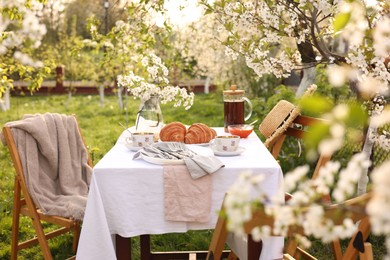 Photo of Stylish table setting with beautiful spring flowers, tea and croissants in garden