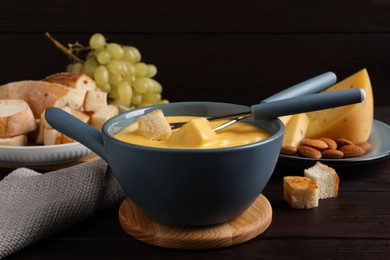 Photo of Pot of tasty cheese fondue and forks with bread pieces on wooden table