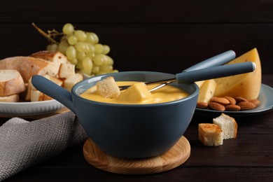 Pot of tasty cheese fondue and forks with bread pieces on wooden table