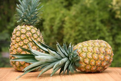 Photo of Delicious ripe pineapples on wooden table outdoors, space for text