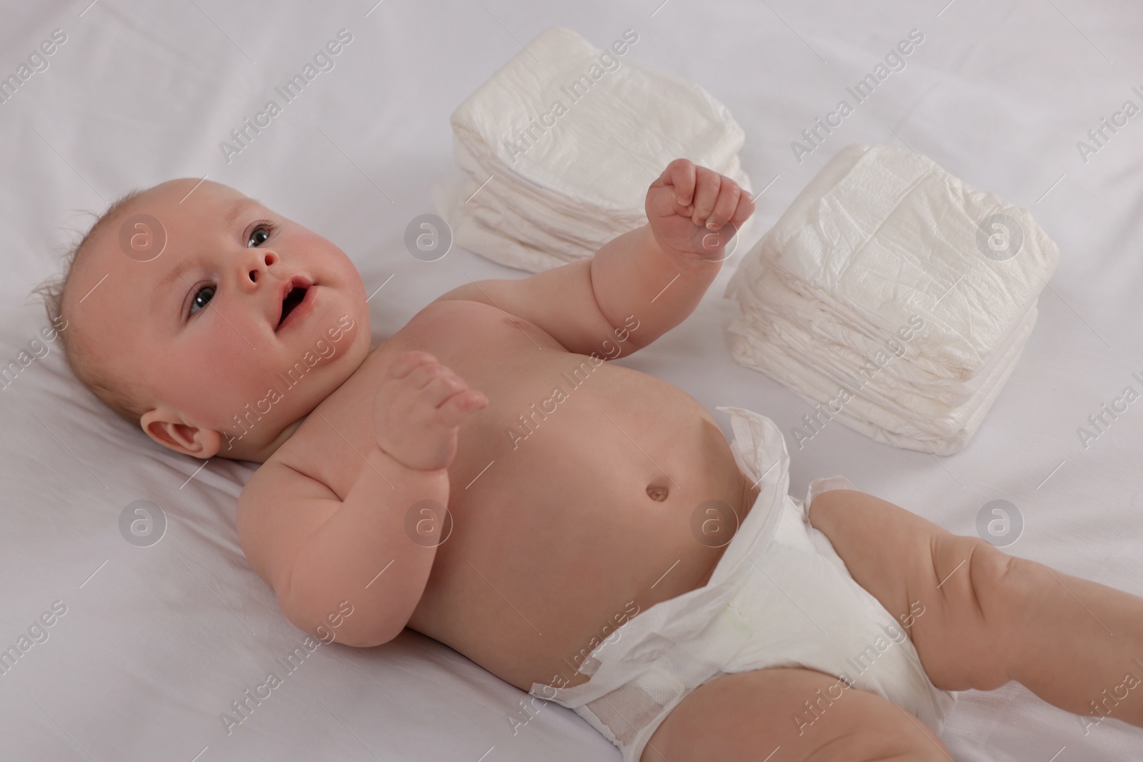 Photo of Cute little baby lying near stack of diapers on bed