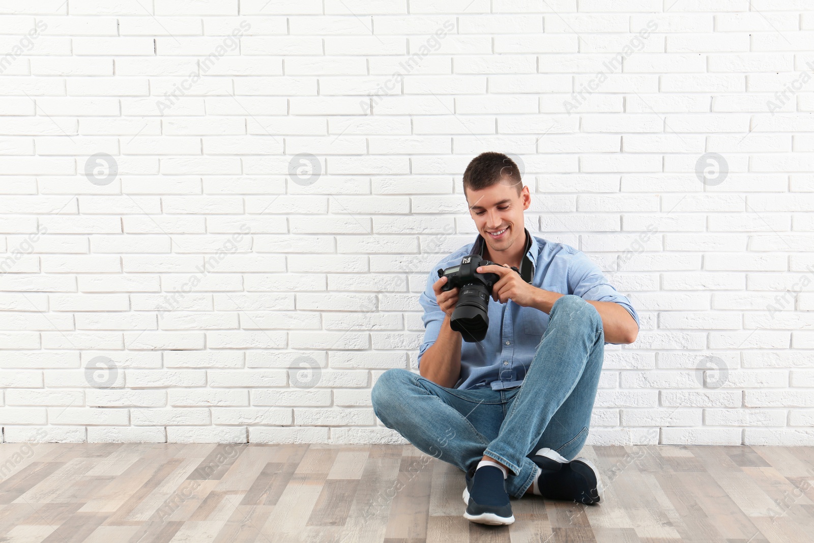 Photo of Young photographer with professional camera near brick wall. Space for text