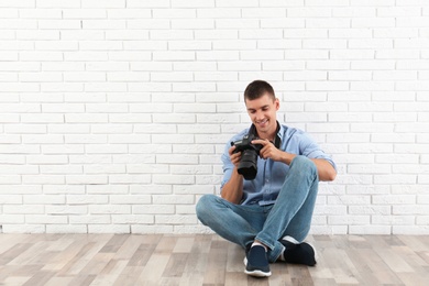 Photo of Young photographer with professional camera near brick wall. Space for text