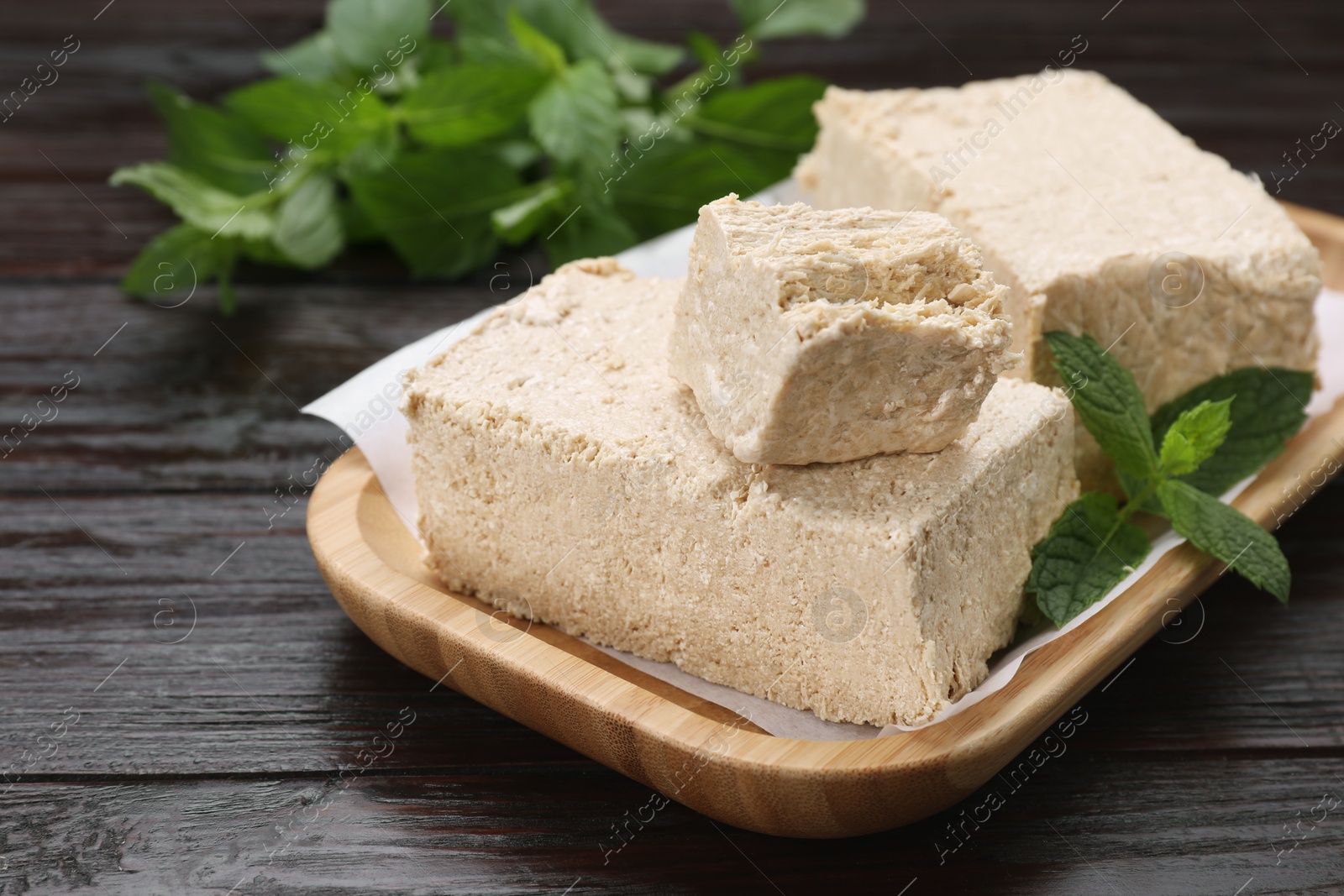 Photo of Pieces of tasty halva and mint on wooden table, closeup