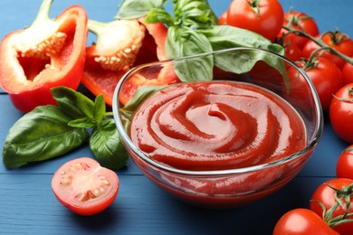 Bowl of tasty ketchup and ingredients on blue wooden table, closeup