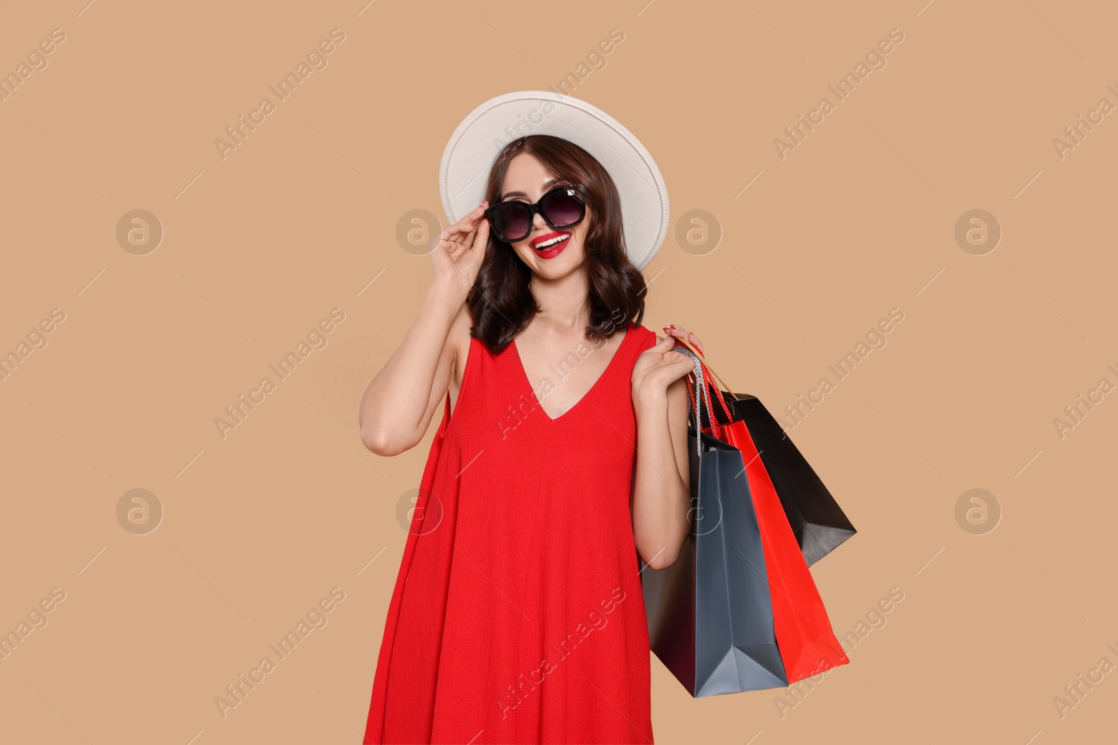 Photo of Beautiful young woman with paper shopping bags on beige background