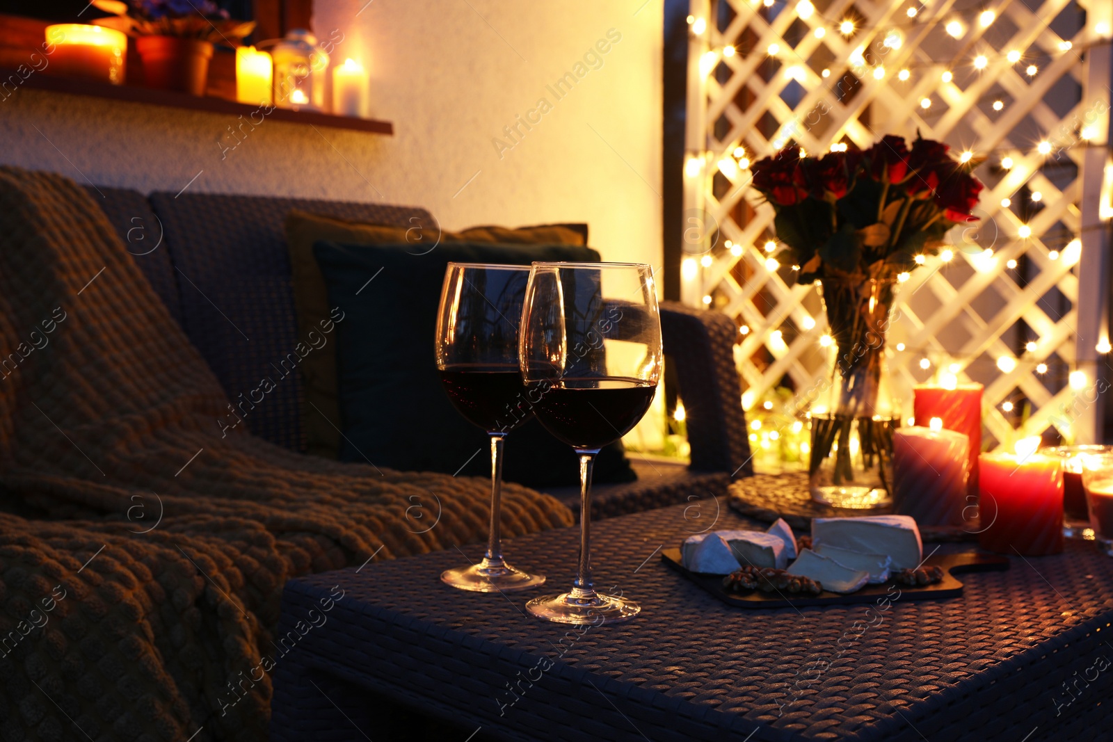 Photo of Glasses of wine, vase with roses, burning candles and snacks on outdoor terrace in evening