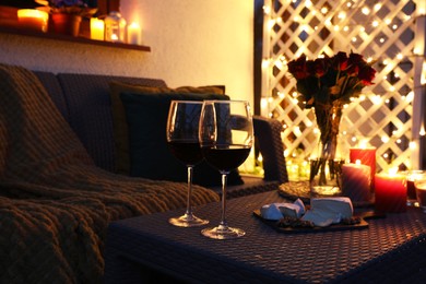 Glasses of wine, vase with roses, burning candles and snacks on outdoor terrace in evening