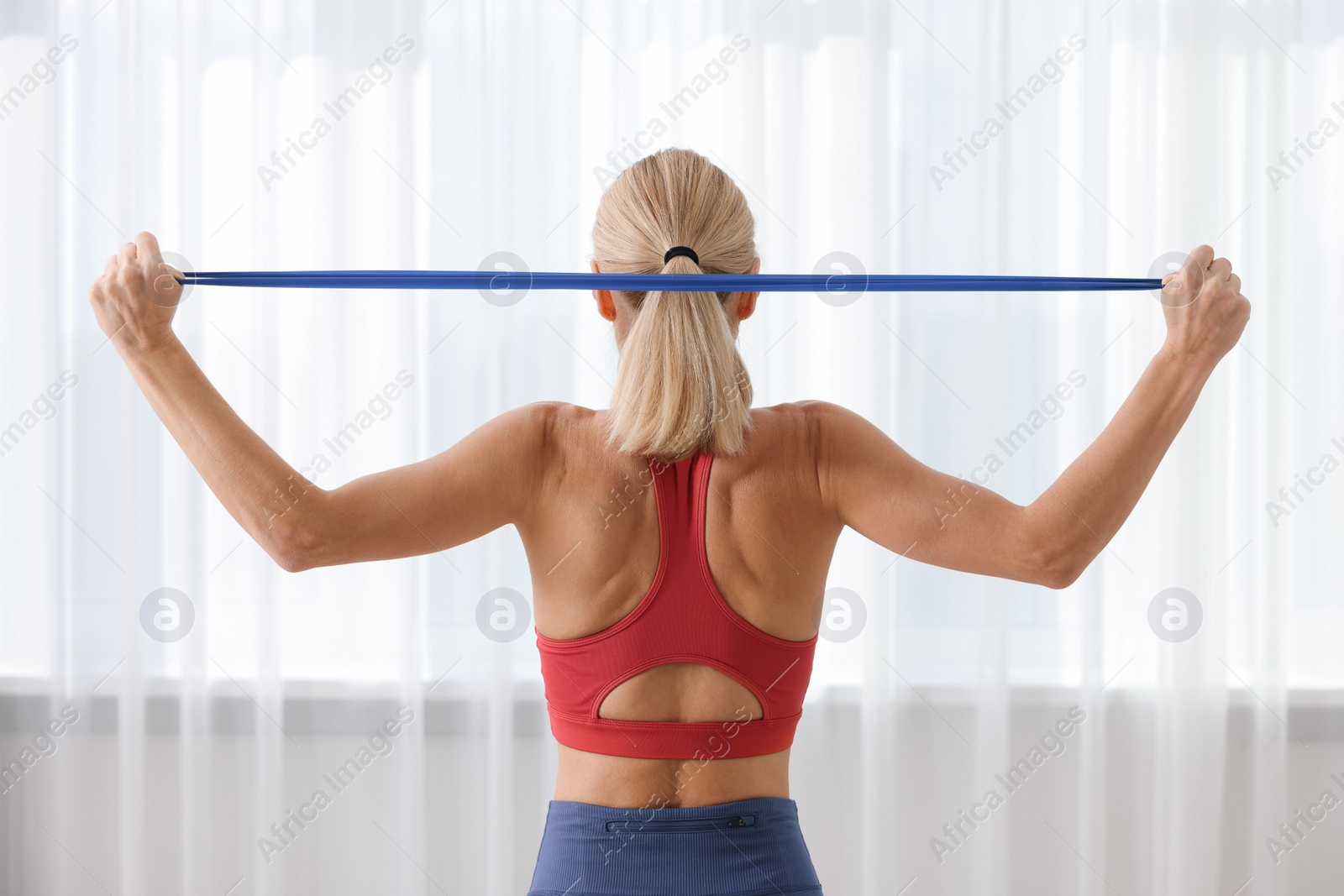 Photo of Fit woman doing exercise with fitness elastic band indoors, back view