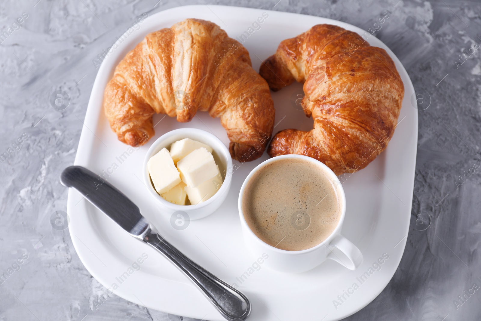 Photo of Tasty breakfast. Cup of coffee, fresh croissants, knife and butter on grey table, above view