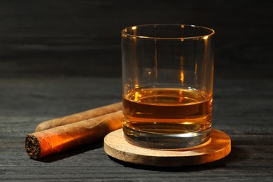 Photo of Glass of whiskey and cigars on black wooden table