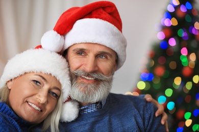 Happy mature couple in Santa hats celebrating Christmas at home