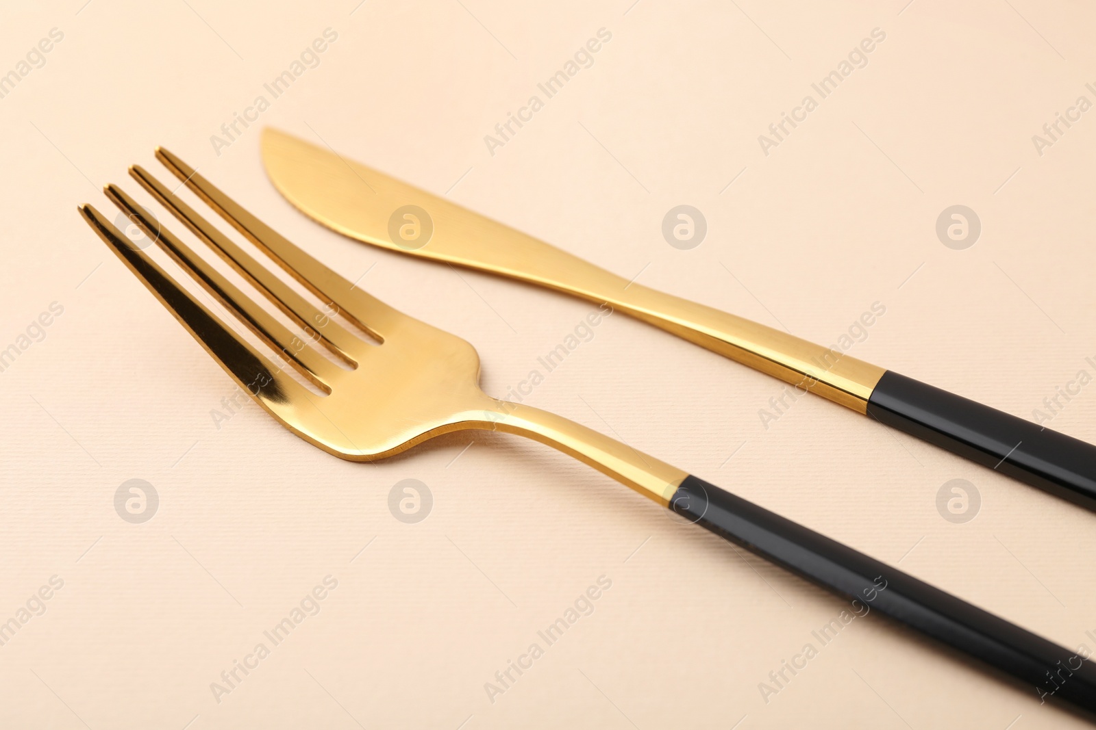 Photo of Stylish cutlery. Golden knife and fork on beige background, closeup