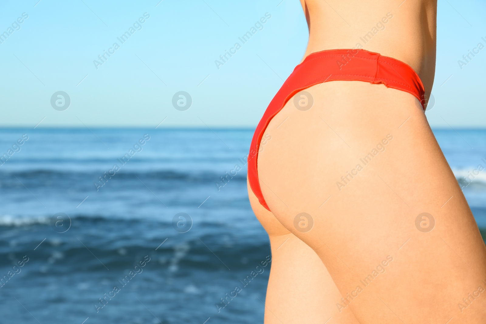 Photo of Young woman in red bikini near sea, closeup. Space for text