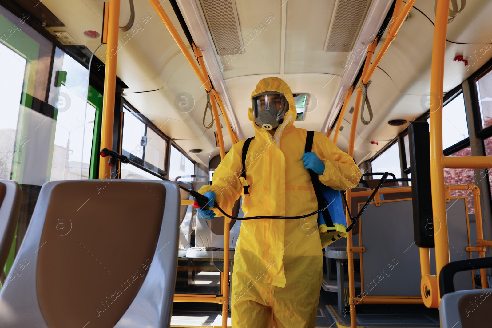 Photo of Public transport sanitation. Worker in protective suit disinfecting bus salon