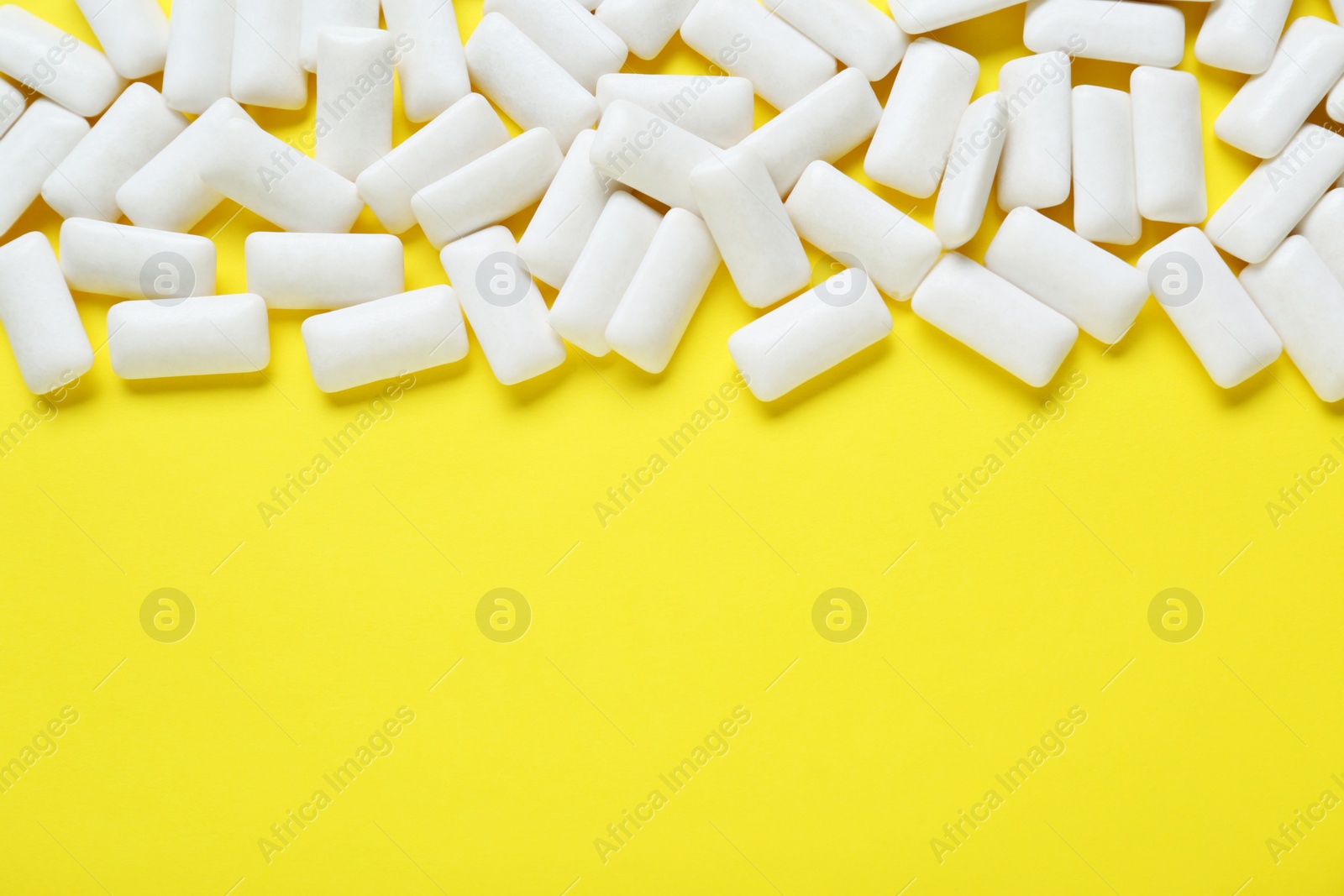 Photo of Tasty white chewing gums on yellow background, flat lay. Space for text